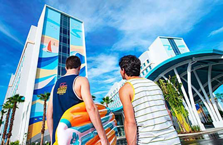 Two guys walk toward universal endless summer surfside inn and suites resort carrying a surf board.