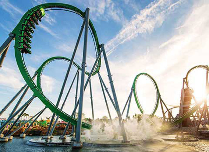 Giant green roller coaster at universal is going around a loop with a group of people.