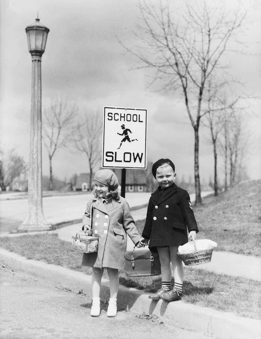 UNITED STATES - CIRCA 1940s:  Boy and girl walking to school, about cross street by 'slow school' sign.