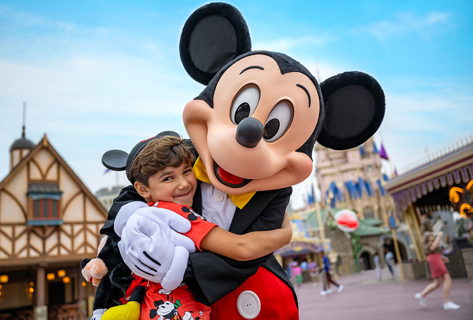 Mickey mouse hugs a little boy in mickey mouse ears.