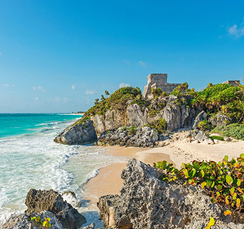 A Mayan or Aztec ruins on a cliff overlooking a sandy beach.